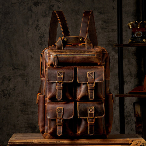 A vintage-style leather backpack with multiple front pockets, displayed against a dark textured background. The bag features brass accents and adjustable straps.