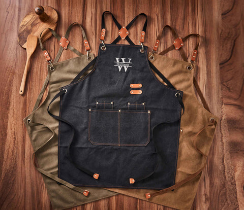 Three canvas aprons (magy green, brown，black), flat lay with wooden kitchen utensils, wooden background