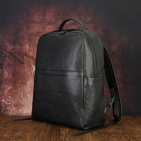 Men’s black leather laptop backpack with top handle and front pocket, displayed on wooden table.