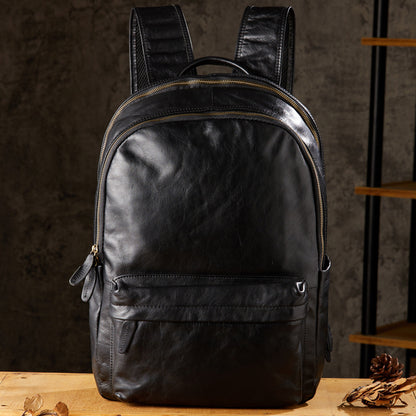 Black leather backpack, vintage style, front view with zipper pocket, on wooden table
