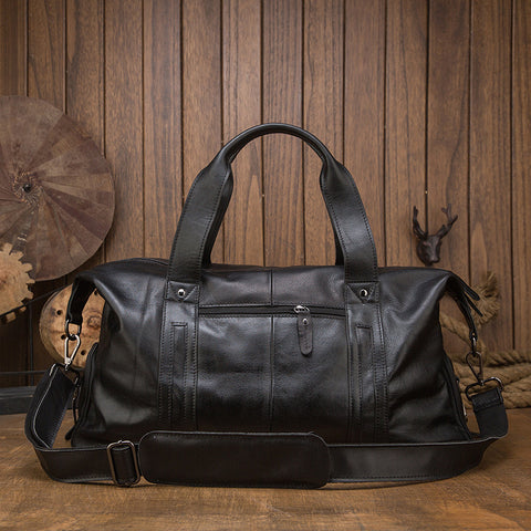 Vintage black leather duffel bag, front view with top handles and shoulder strap, wooden background