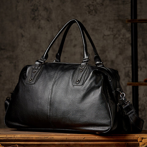 Black leather duffel bag, front view, classic duffel shape, rustic setting