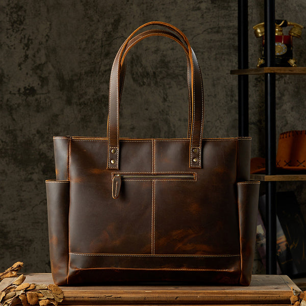 Brown leather tote bag with front zipper pocket, classic design, rustic setting
