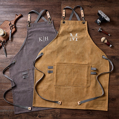 Two canvas aprons (gray and kakhi), flat lay with barber tools, wooden background