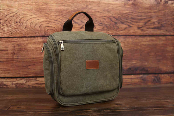 Army green canvas toiletry bag, front view with leather patch, wooden background