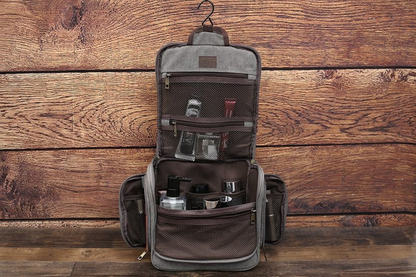 Grey canvas toiletry bag, fully open with hanging hook, multiple compartments filled with grooming products, wooden background
