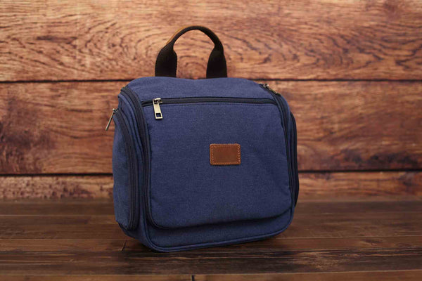 Blue canvas toiletry bag, front view with leather patch, wooden background