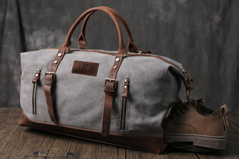 Gray canvas duffle bag with brown leather accents, personalized "JKM" patch, and brown shoes
