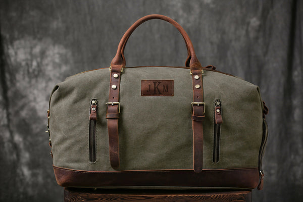 Olive green canvas duffle bag with brown leather accents, personalized "JKM" patch
