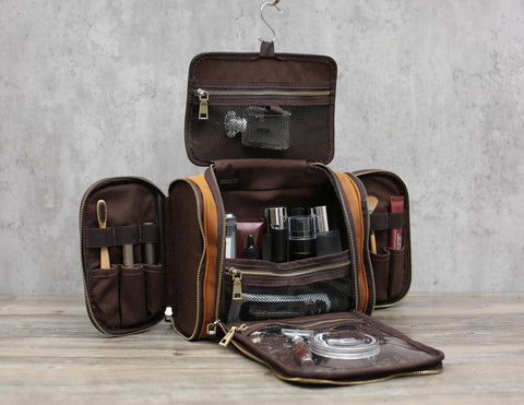 Brown leather toiletry bag, fully open with multiple compartments, filled with grooming products and tools