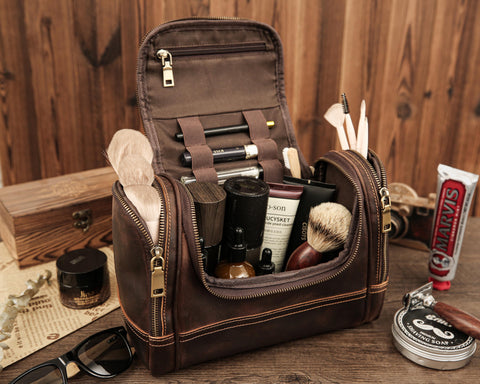 Dark brown leather toiletry bag with multiple compartments, filled with grooming tools, brushes, and skincare products