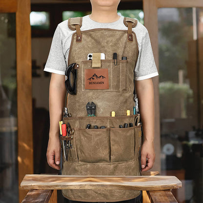 Man wearing khaki work apron with "Benjamin" logo, tool pockets, workshop background