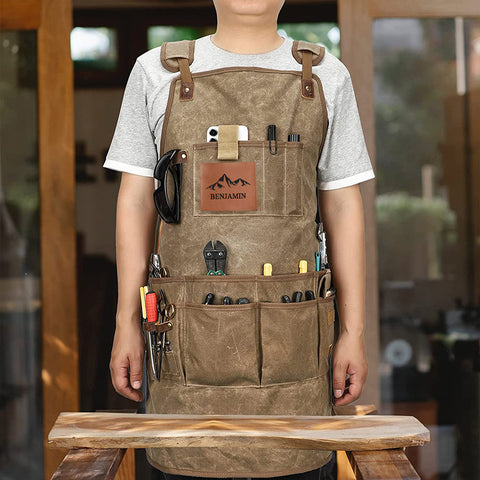 Man wearing khaki work apron with "Benjamin" logo, tool pockets, workshop background