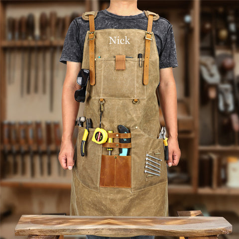 Man wearing personalized brown canvas work apron with "Nick" embroidery, tool pockets, workshop background