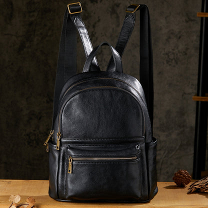 Black leather backpack with multiple zipper pockets, vintage style, front view on wooden table